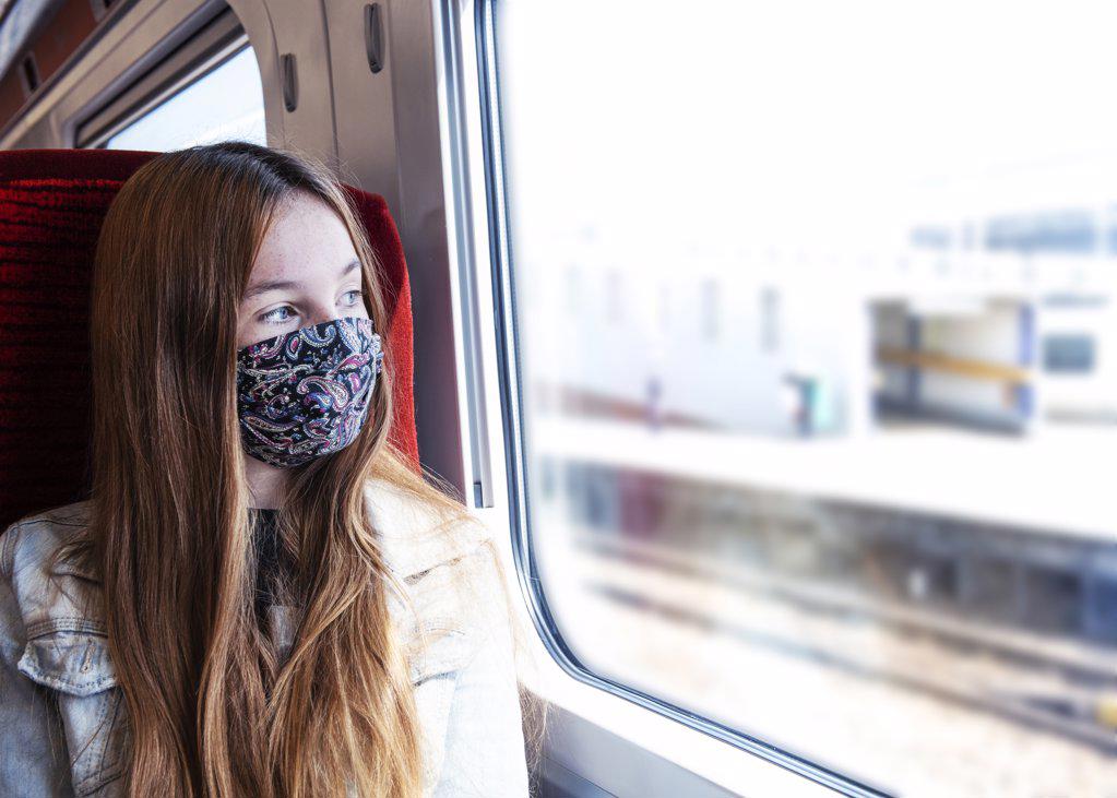 Young teenager looking concerned travelling on a train wearing a mask