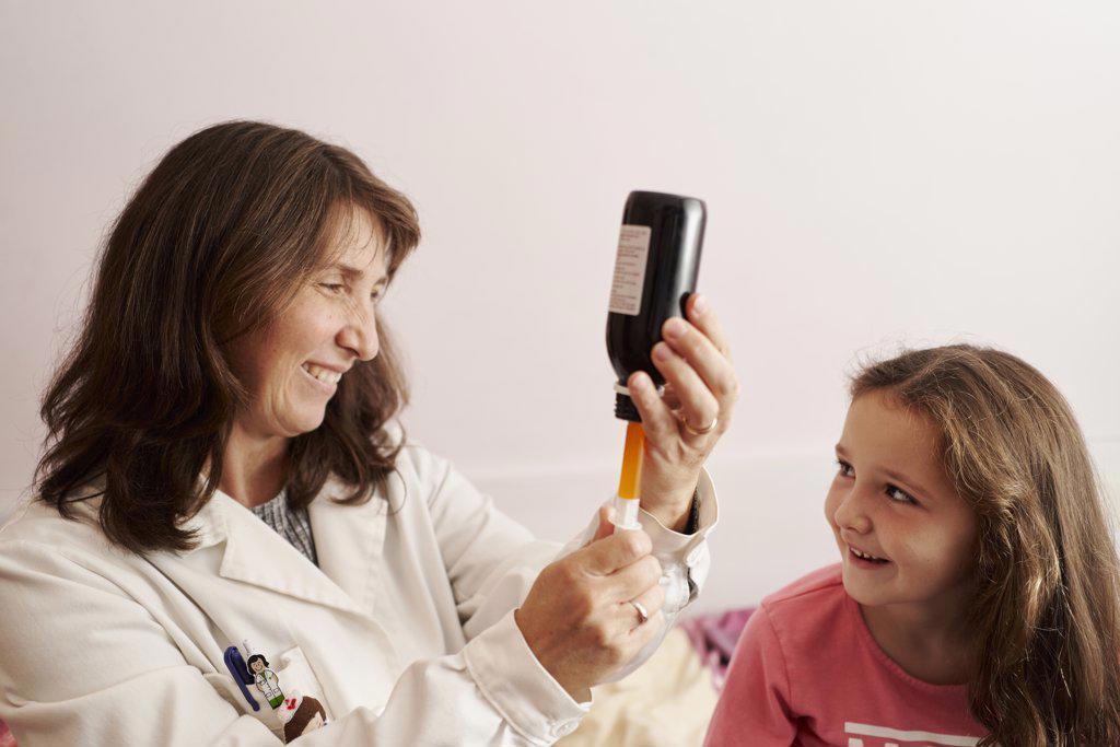 Female doctor giving syrup with syringe to a little girl at home. Home doctor concept