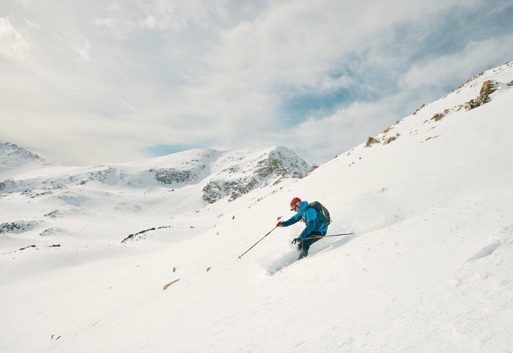 Male skier skis down a powdery slope on a sunny day in the backcountry