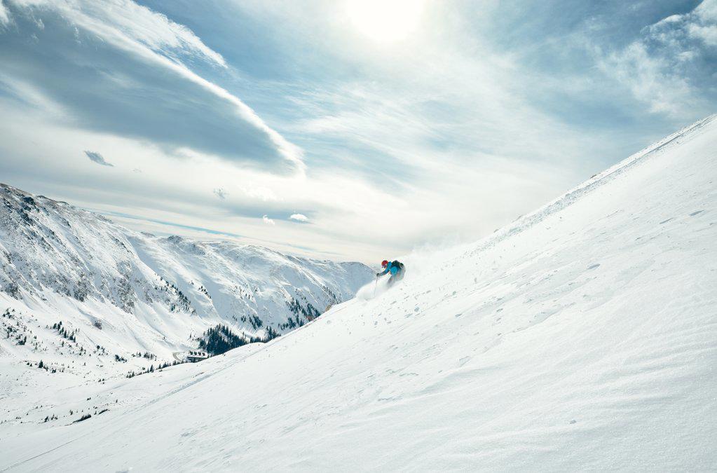 Male skier skis down a powdery slope on a sunny day in Colorado