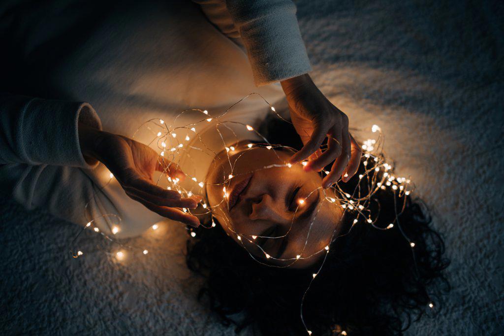 Woman lying down in bed with tangled string lights in her hair