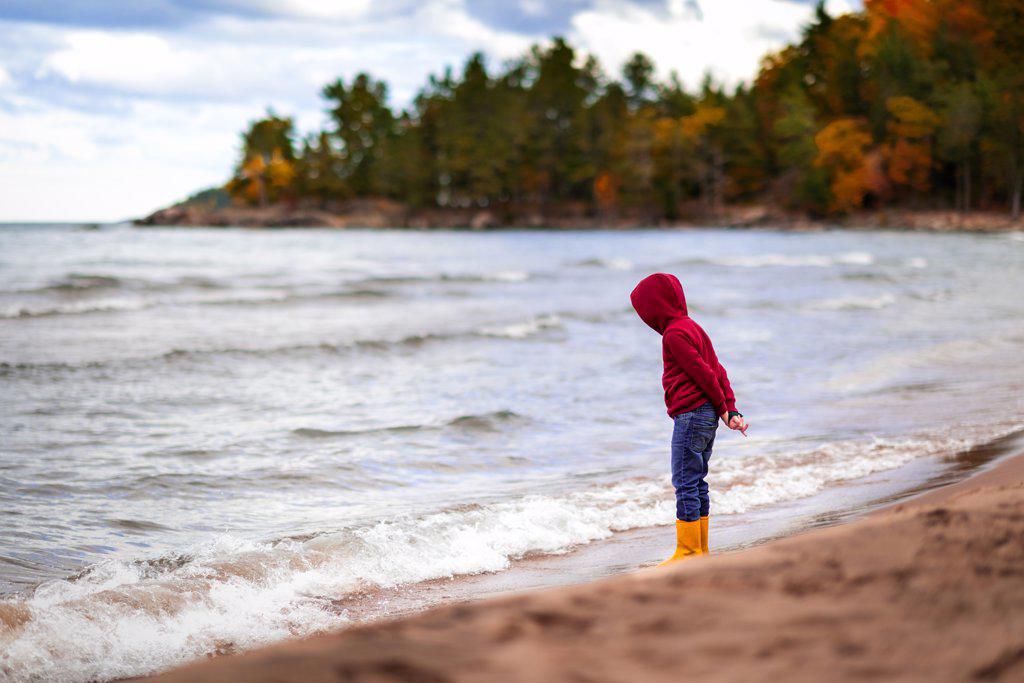 boy standing on shore line of Lake Superior looking down at water