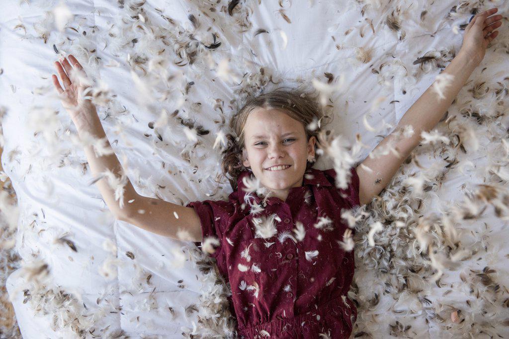 Young blond girl laying on the bed during a feather pillow fight.