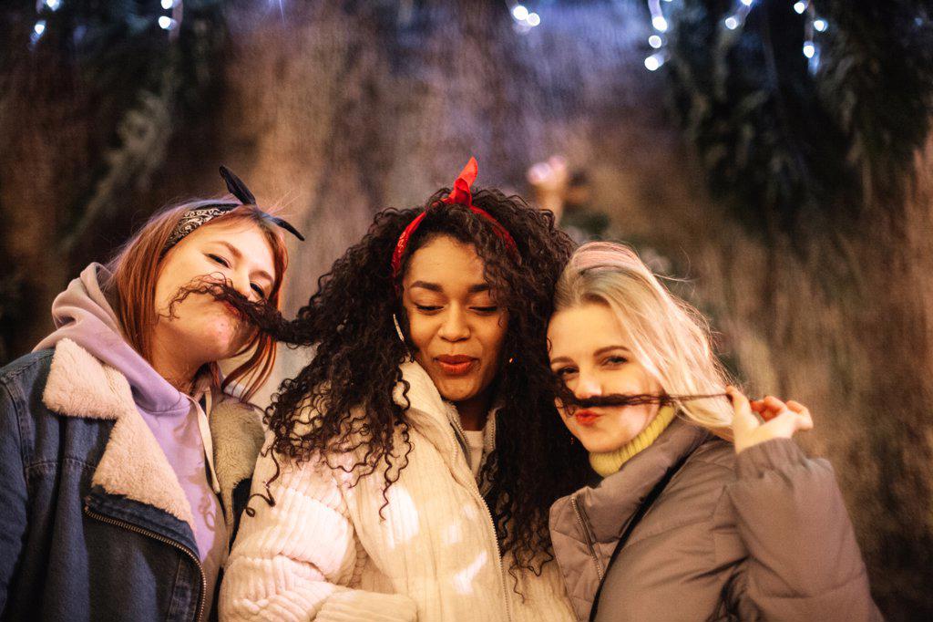 Young women making fake mustaches with their girlfriendâ€™s hair in city