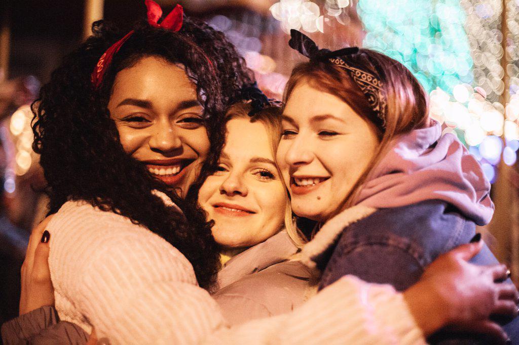 Close up portrait of happy female friends embracing in city at night