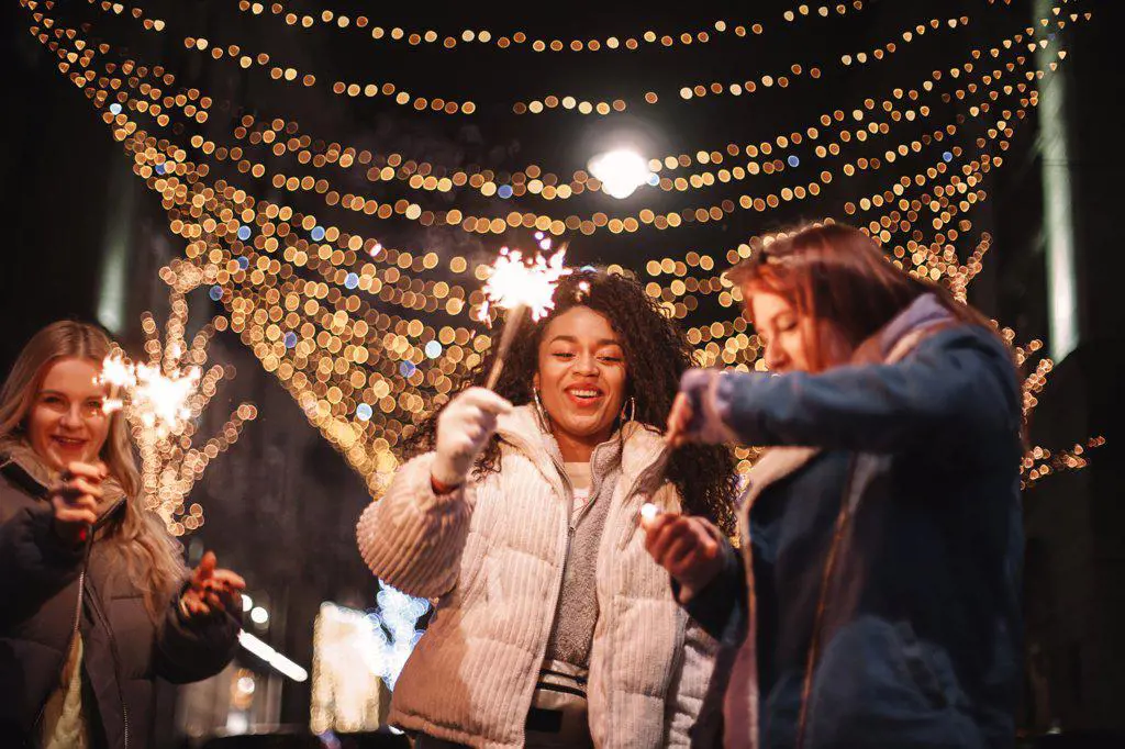Happy young women holding sparklers standing in city during Christmas