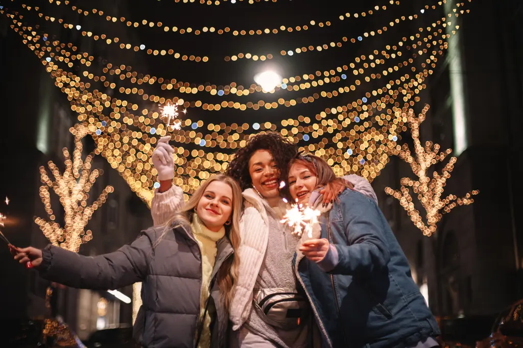 Happy female friends holding sparklers in city during Christmas