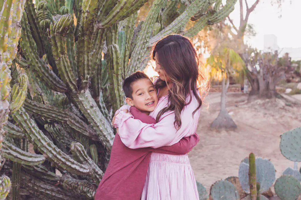 Mother hugging son in front of a big cactus with back light sun.