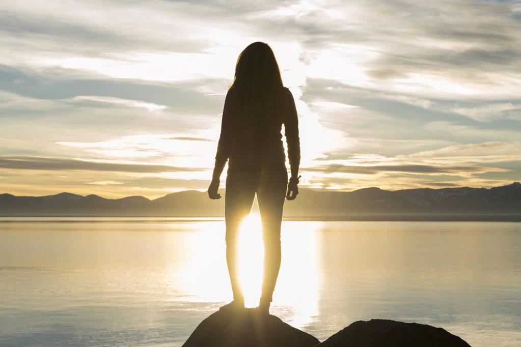 Young adventurous women standing on rock overlooking Lake Tahoe sunset