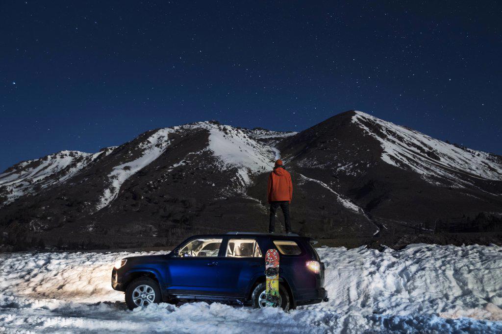 Male standing on top of SUV during winter looking at stars