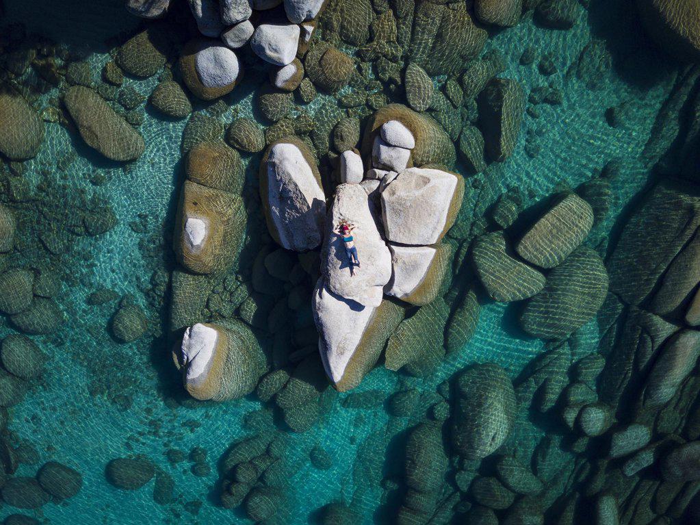 aerial view female laying on rock in lake tahoe