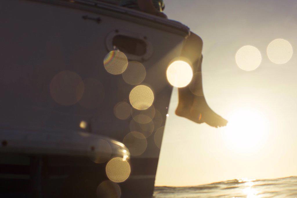 feet hanging over boat at sunset