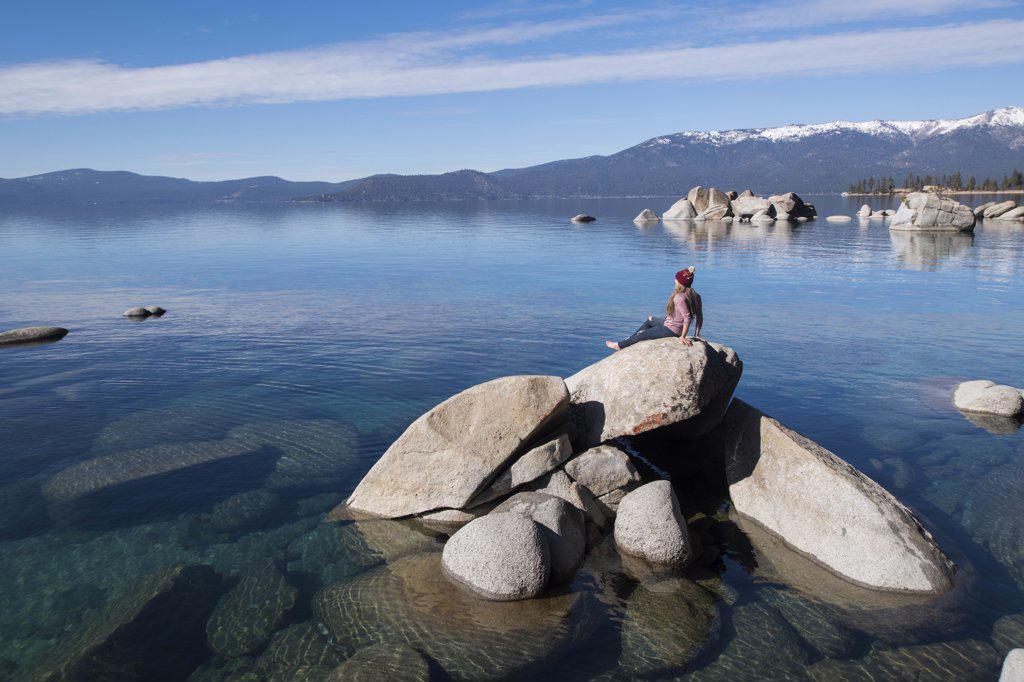 young female sitting on rock in lake tahoe on sunny afternoon