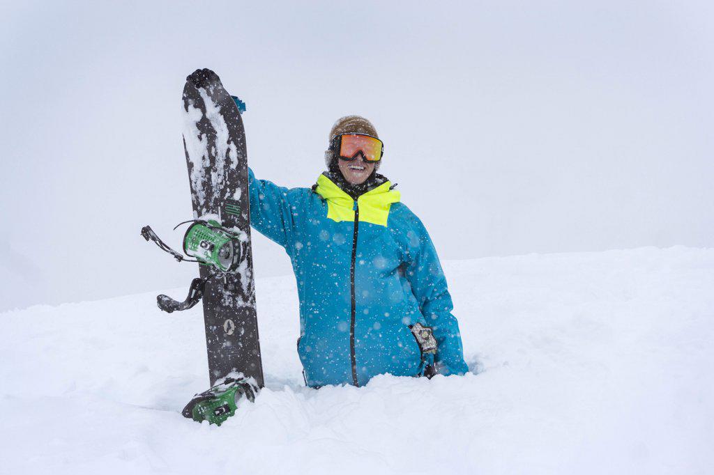 young male standing with snowboard in deep snow in the mountains