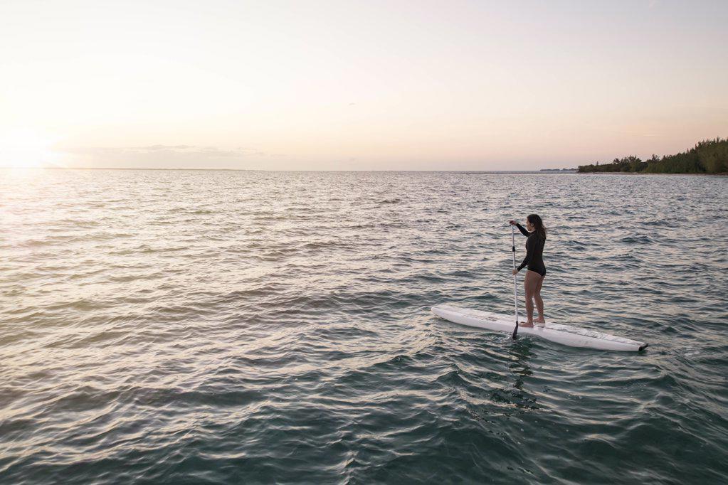 young asian female paddleboarding in Bahamas at sunset