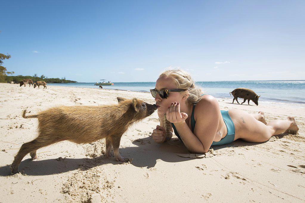 Young blonde female kissing pig on beach in Bahamas