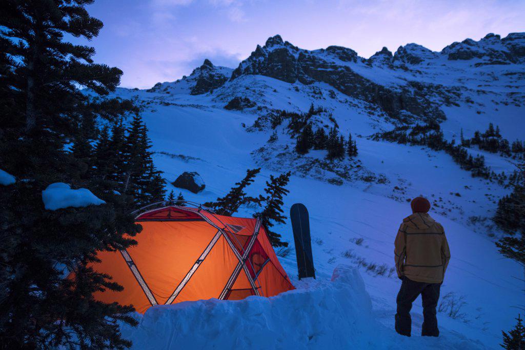 Young male standing outside tent at twilight in winter