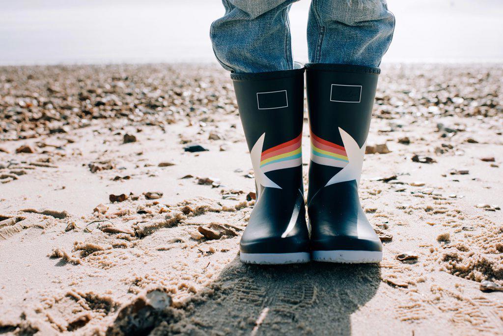 child's feet in rain boots on a sandy beach in the sunshine