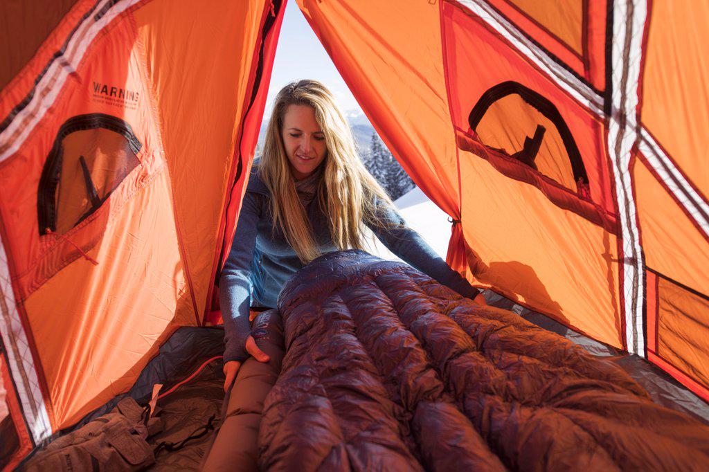 Young female setting up sleeping bag in tent while winter camping