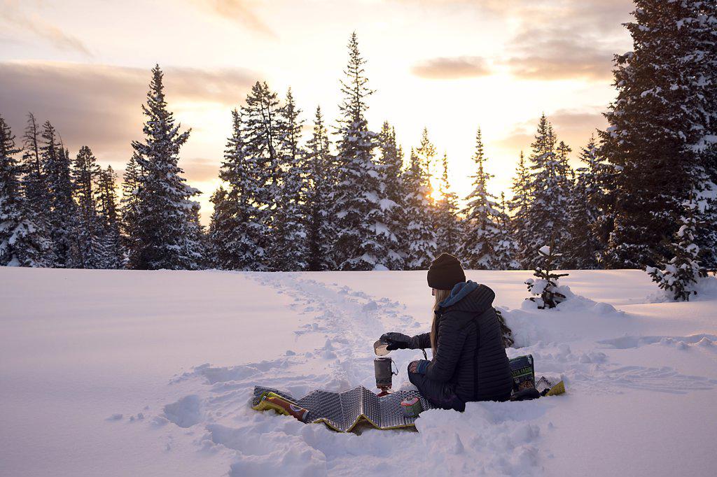 Young female making dinner while winter camping at sunset