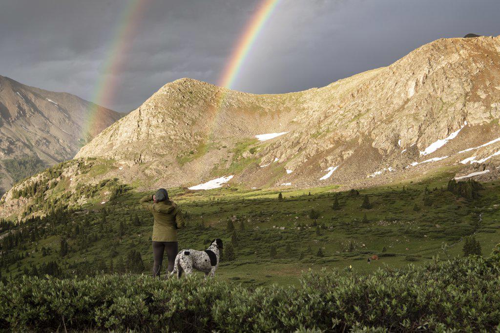 Rear view of woman looking at double rainbow while hiking with dog during vacation