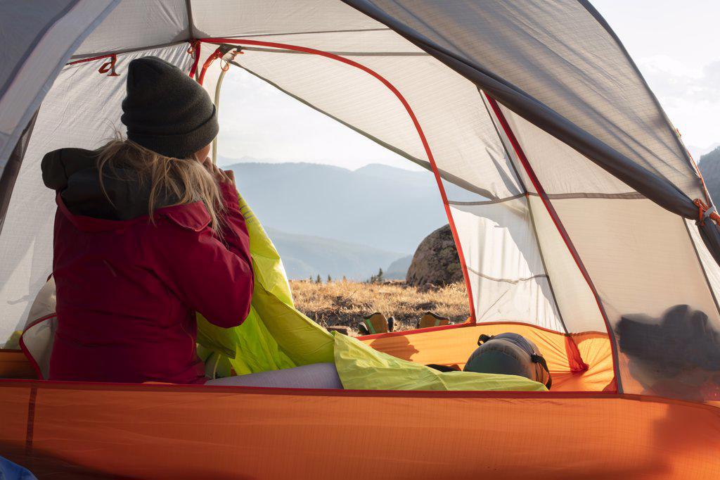 Rear view of woman blowing mattress while sitting in tent on mountain during vacation