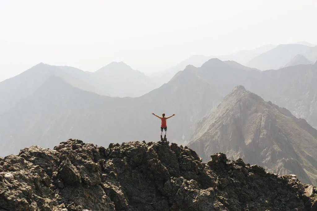 Woman standing with arms outstretched on peak of mountain against clear sky