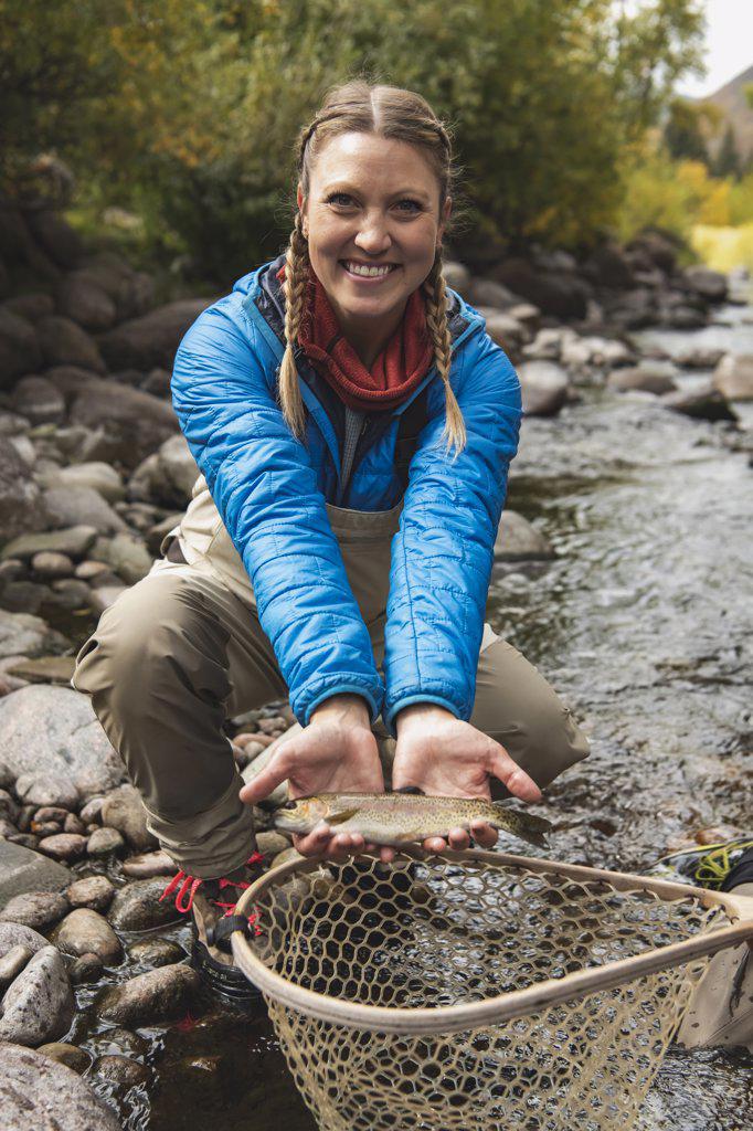 Portrait of smiling young woman with fish catch at stream in forest