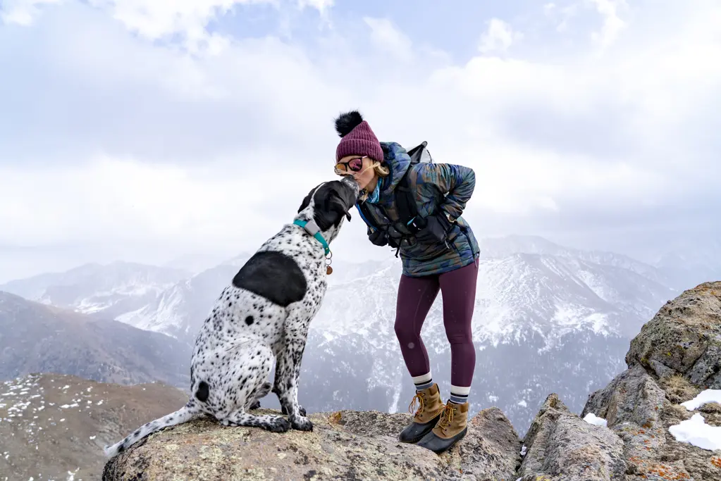 Young woman kissing dog on mountain peak while hiking during vacation