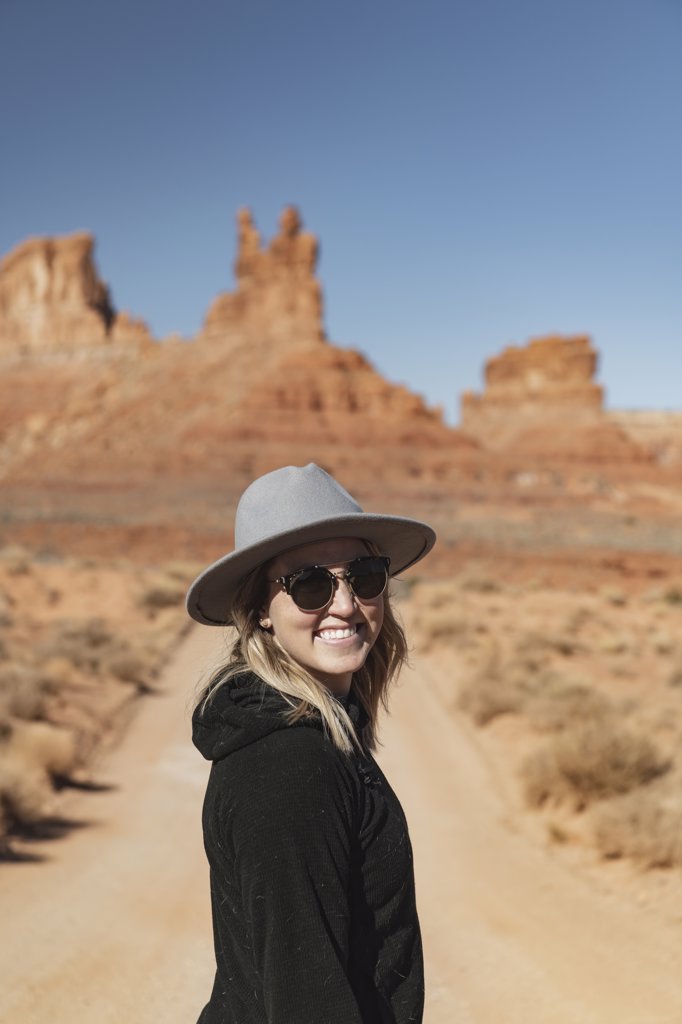Portrait of smiling young woman in sunglasses standing on dirt road at desert