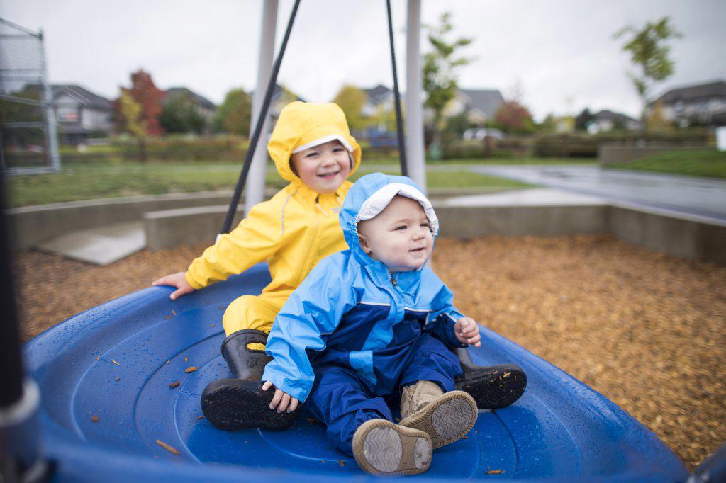 Two kids sit on a large blue swing at the park