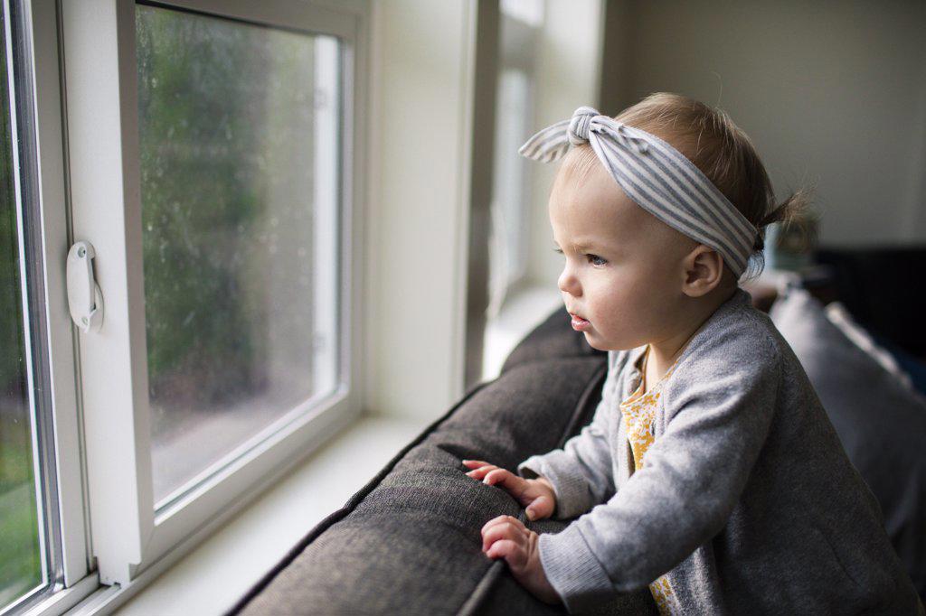 Pretty young girl looking out window from inside her home.