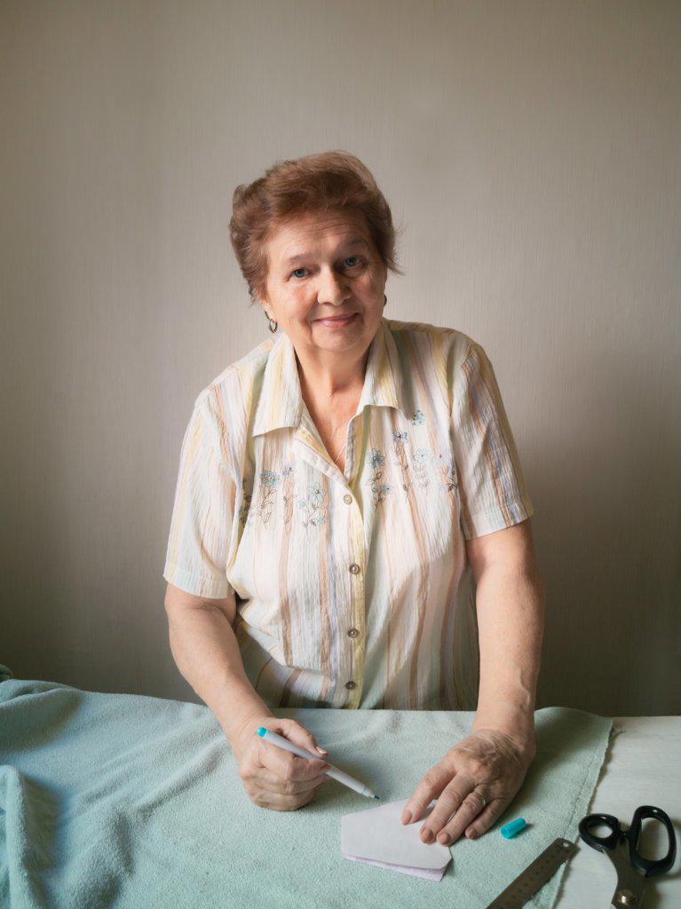 An elderly woman makes a pattern of a medical mask on a fabric