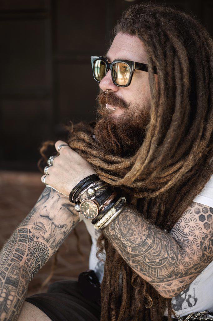 hipster guy with dreadlocks and tattoo sitting on the beach in thailan