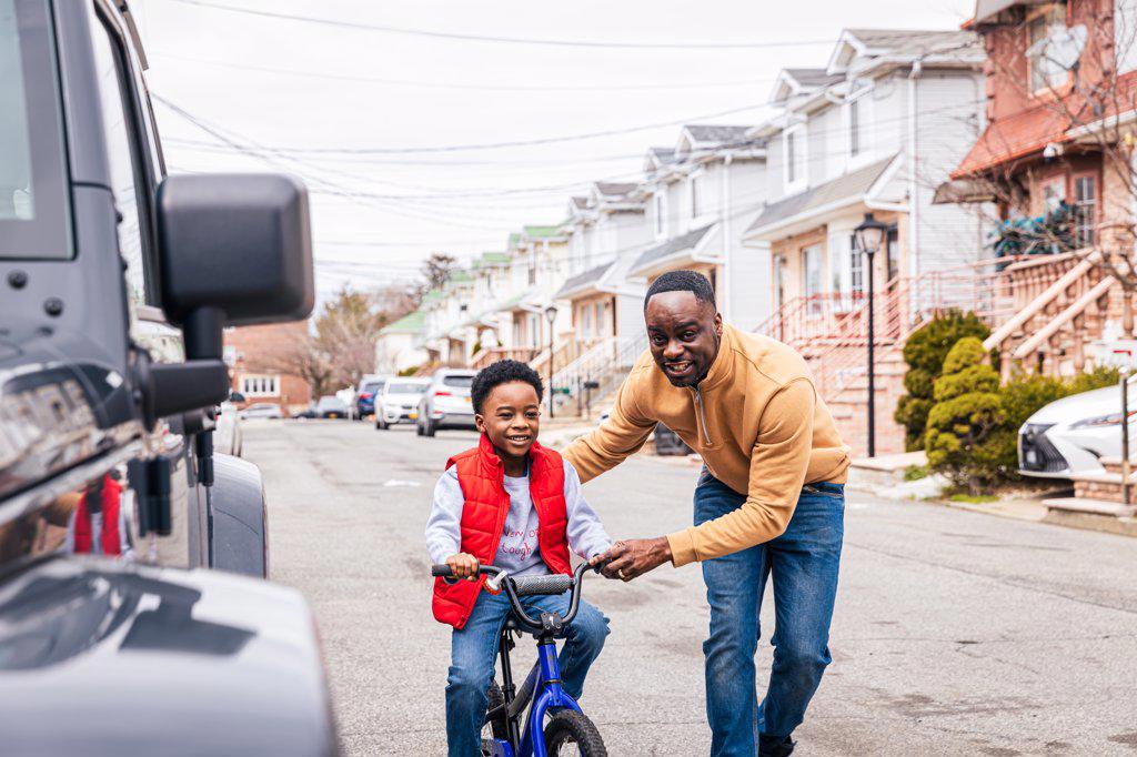 Smiling father helping son to ride a bike on the street outside