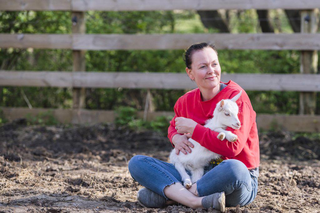 Woman in red sweatshirt holding a white baby goat on her lap.