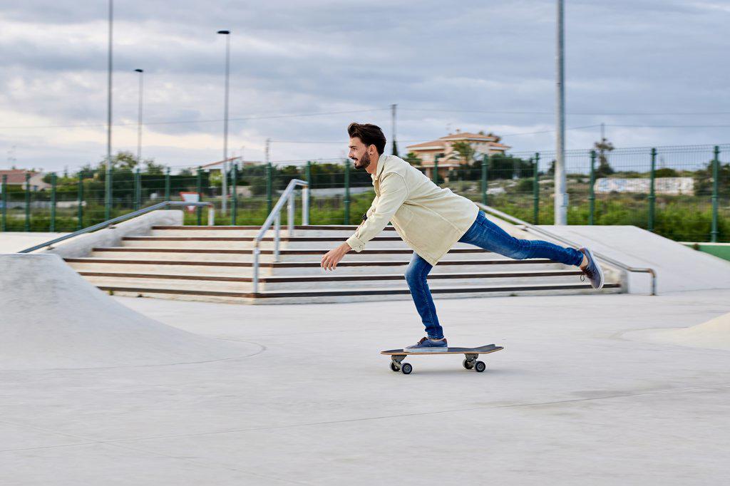 Young man skates at a skate park in casual clothes