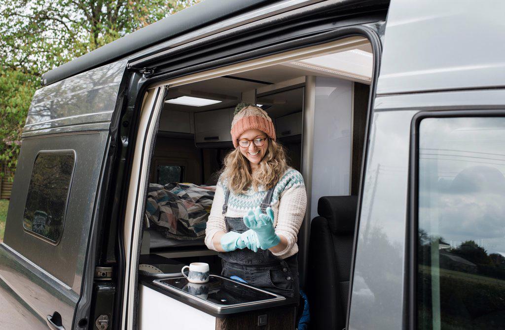 woman putting rubber gloves on in her camper van washing up happily