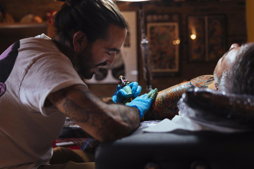 Tattoo artist enjoys while working on a customer's arm in his studio.