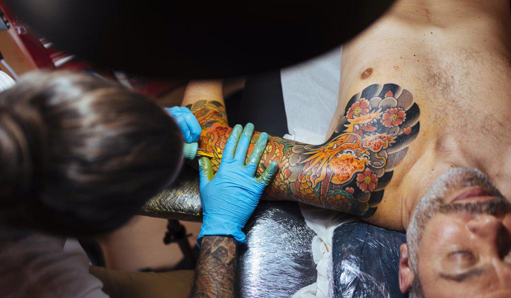 Aerial view of an tattoo artist working on a customer's arm.