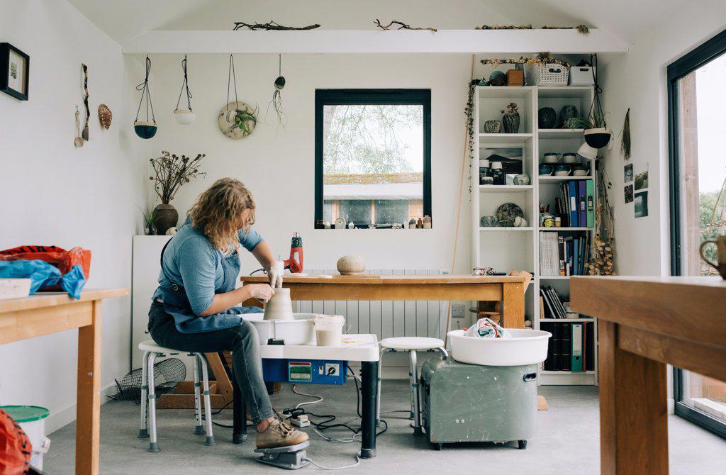 woman spinning clay on a pottery wheel in her home studio office in UK