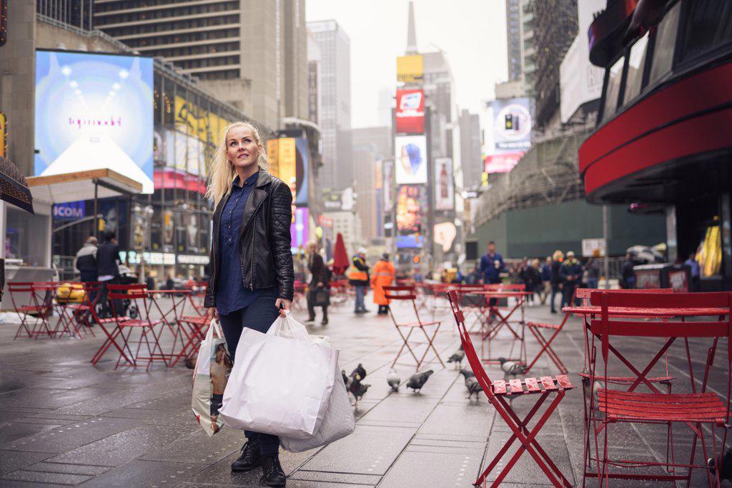 Positive woman with shopping bags standing on rainy Times Square