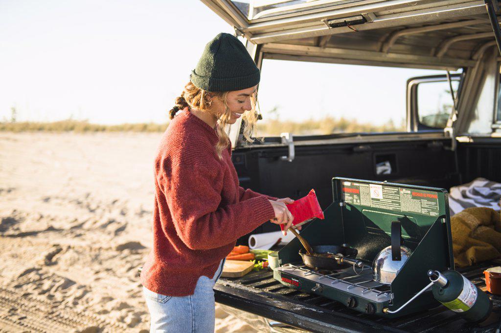 Young woman tailgate cooking while beach car camping alone