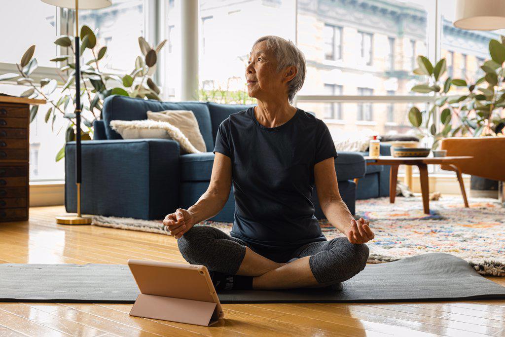Senior woman meditating while learning through digital tablet at home