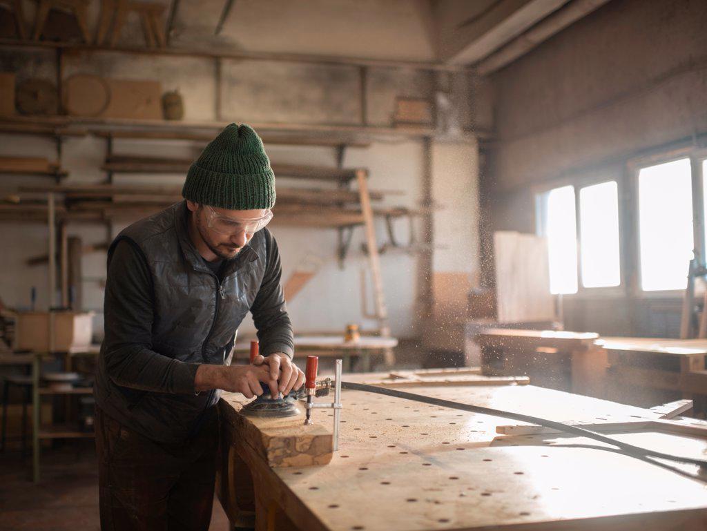 Male carpenter polishing wooden plank