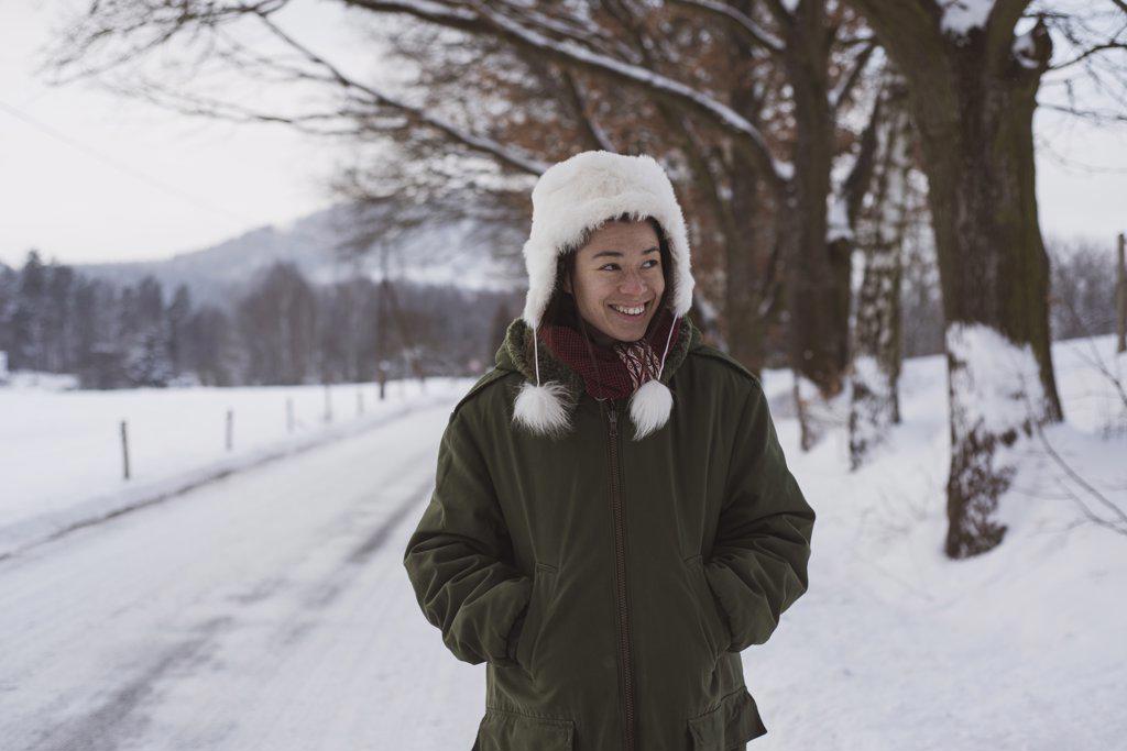 Chinese person in fluffy snow hat smiles and walks along winter road