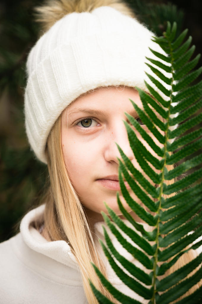 Young Girl Wearing Winter Hat Holding Green Fern in Front of Face