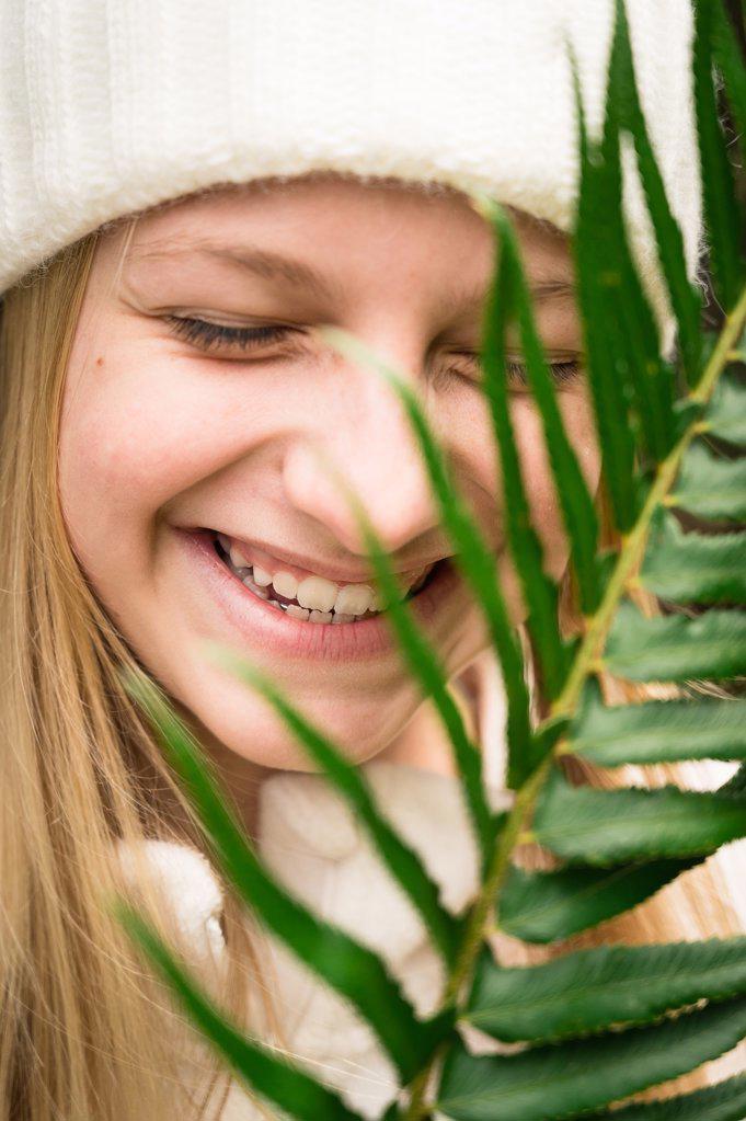 Young Girl in Winter Hat Laughing Behind Green Fern