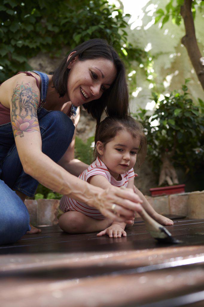 mother and daughter laugh as they paint the wood on the floor