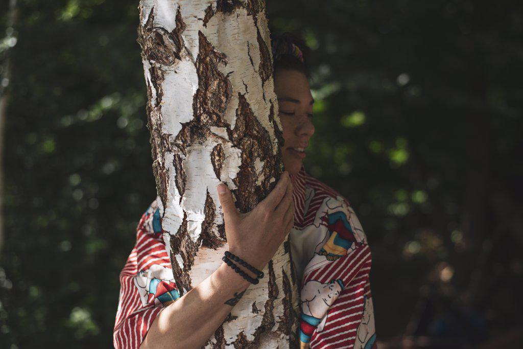 Non-binary person in colourful shirt hugging a birch tree in summer
